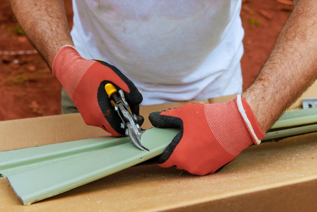 Worker cuts plastic vinyl siding to size with a of scissors before installing it